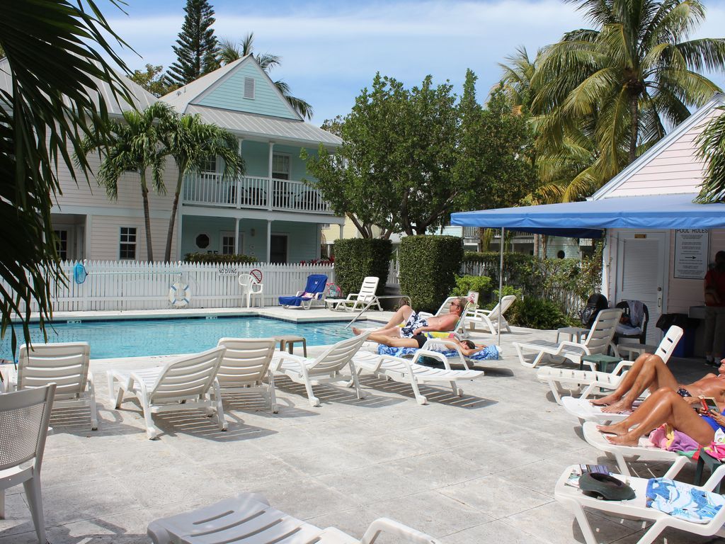 A poolside area with lounge chairs, a pool, and a building with a balcony.