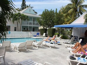 Uma área junto à piscina com espreguiçadeiras, piscina e um edifício com varanda.