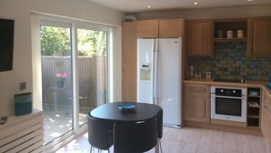 A modern kitchen with a refrigerator, oven, and a dining area with two chairs. - Garden bungalow - dog friendly (Bushey)