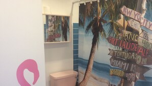 A bathroom with a toilet, a sink, and a wall mural featuring a palm tree and various city names. - Garden bungalow - dog friendly (Bushey)