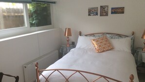 A neatly made bed with white linens and patterned pillows, a copper-framed headboard, a bedside lamp, and artwork on the wall. - Garden bungalow - dog friendly (Bushey)
