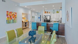 A modern kitchen with white cabinets, a stainless steel refrigerator, and a dining area with a glass table and colorful chairs.