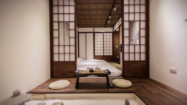 Um quarto japonês tradicional com tatames, uma mesa de madeira baixa com conjunto de chá e uma cama com cabeceira de madeira.