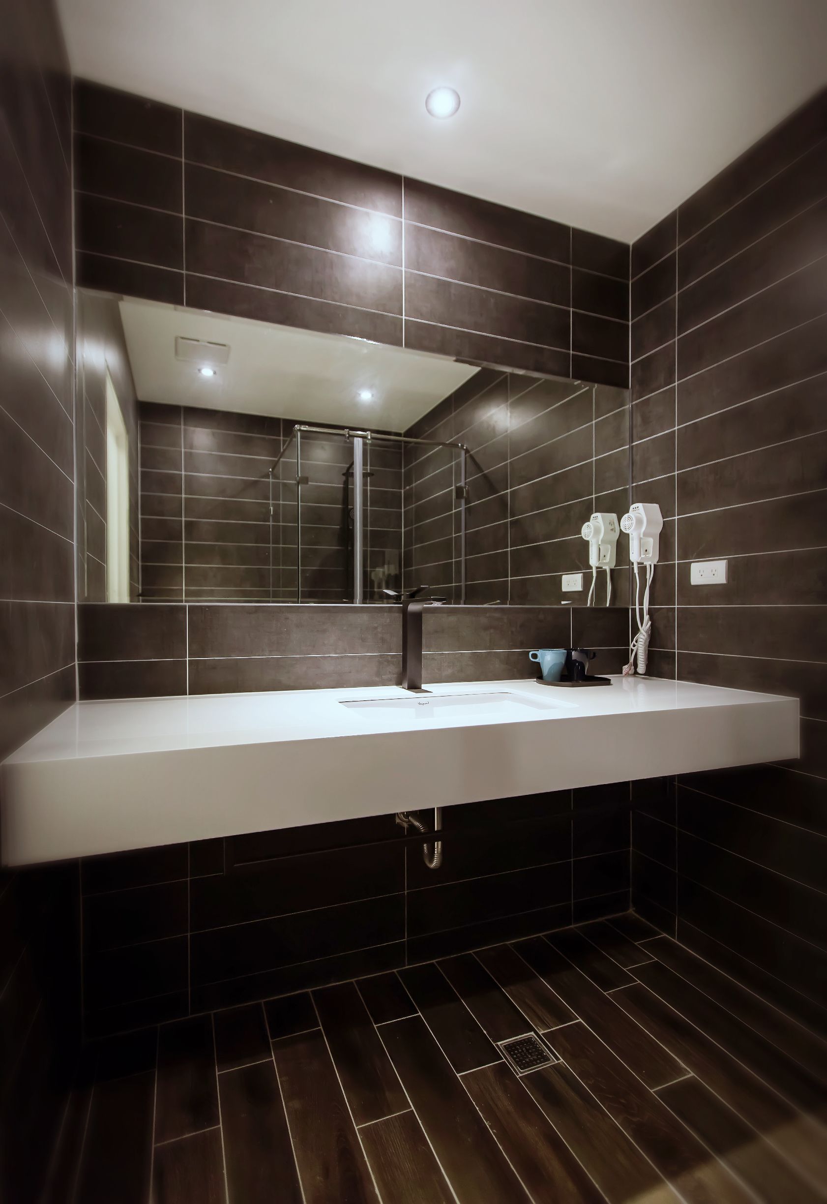A modern bathroom with dark tiled walls, a white sink, and a mirror.