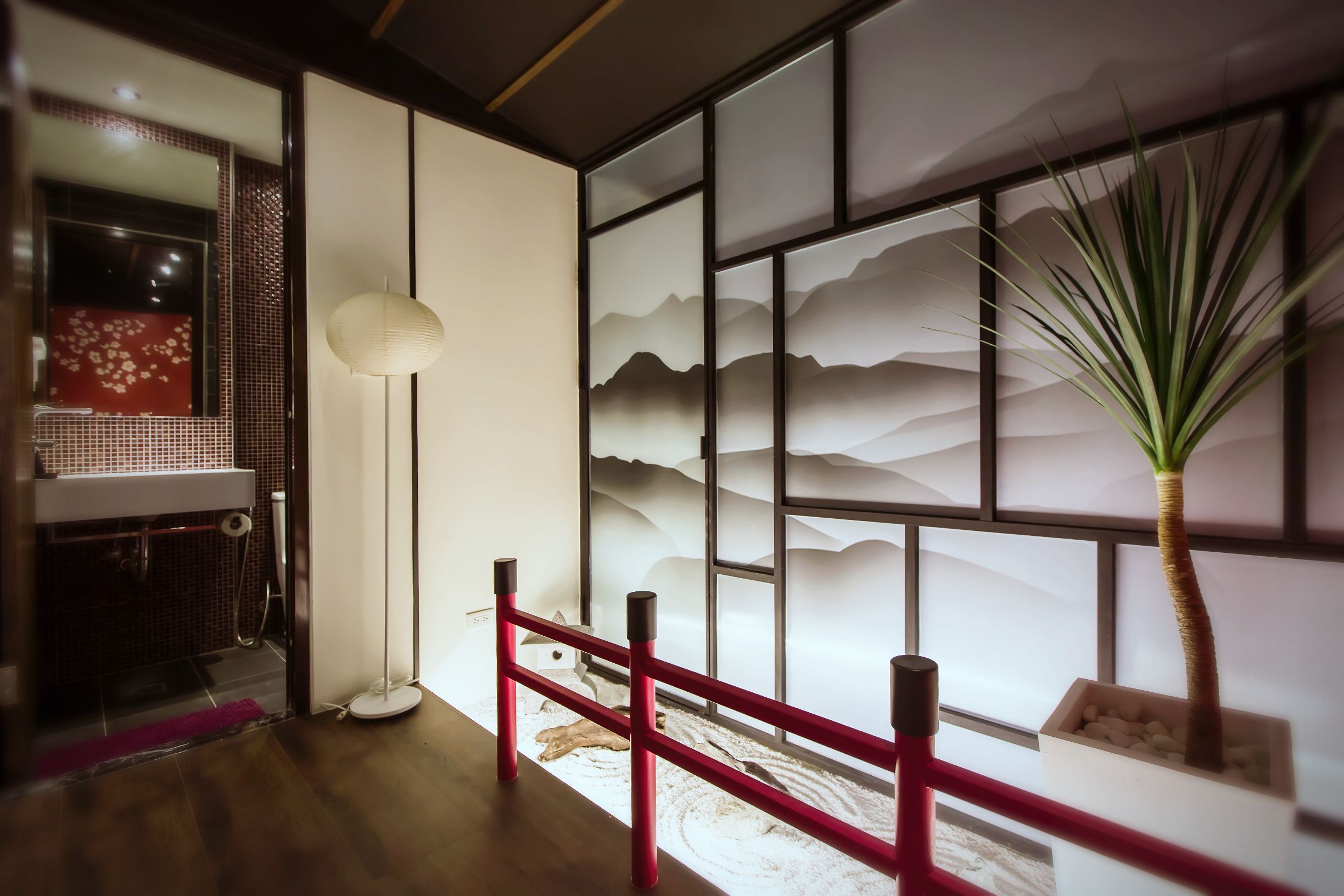 A traditional Japanese room with sliding doors, a tatami mat floor, a red wooden fence, a potted plant, and a decorative wall with mountain patterns.
