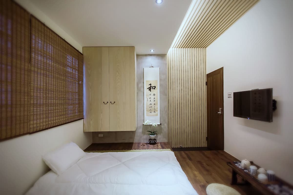 A bedroom with a bed, wooden wardrobe, a wall-mounted TV, and a decorative plant.