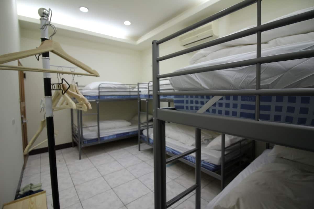 A dormitory room with bunk beds, a metal wardrobe, and a ceiling-mounted air conditioning unit.