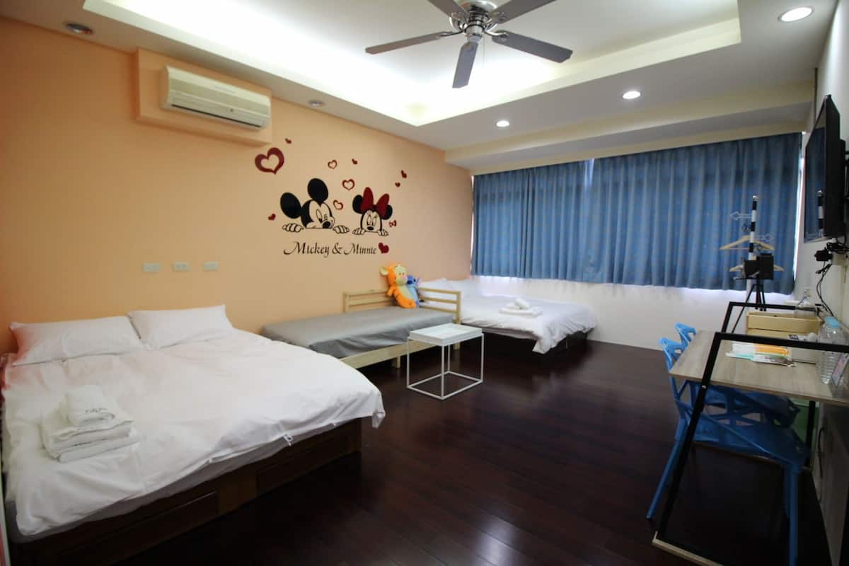 A hotel room with two beds, a desk, and a ceiling fan.