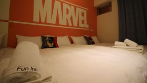 A hotel room with a large 'MARVEL' sign on the wall, a neatly made bed with white linens, and a 'Fun Inn' towel on the bed. - Movie Inn Hostel (Taichung)