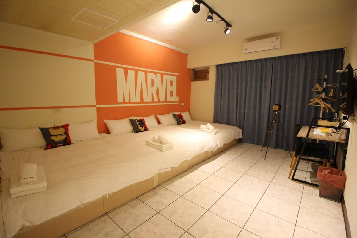 A hotel room with a large bed, a wall with 'MARVEL' branding, a tripod, and a camera on a stand.