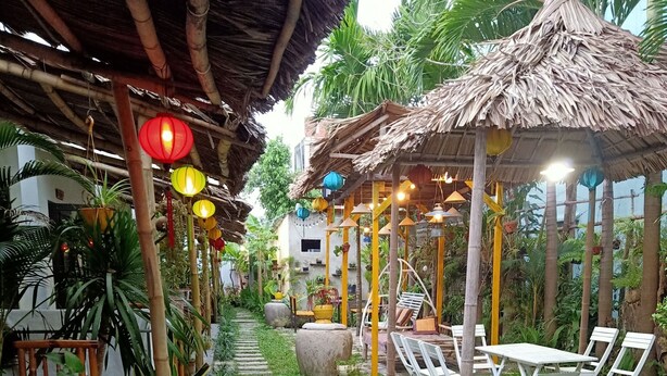 Un jardín con un sendero de piedra, mobiliario exterior y estructuras de techo de paja.