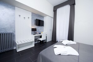 Una habitación de hotel moderna con cama, escritorio, silla, televisor y radiador.