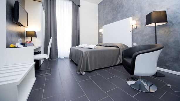 A modern hotel room with a bed, a desk with a chair, a TV, and a lamp. - Grey&White B&B (Rome)