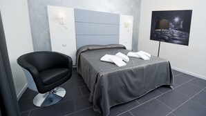A modern hotel room with a grey bed, a black chair, and a wall-mounted TV. - Grey&White B&B (Rome)