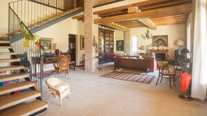 A spacious living area with a staircase, wooden beams, and a fireplace. - Villa Monia (Bettola)