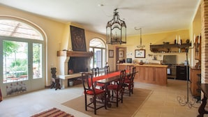 A spacious dining area with a long wooden table and chairs, a fireplace, and a kitchen in the background. - Villa Monia (Bettola)