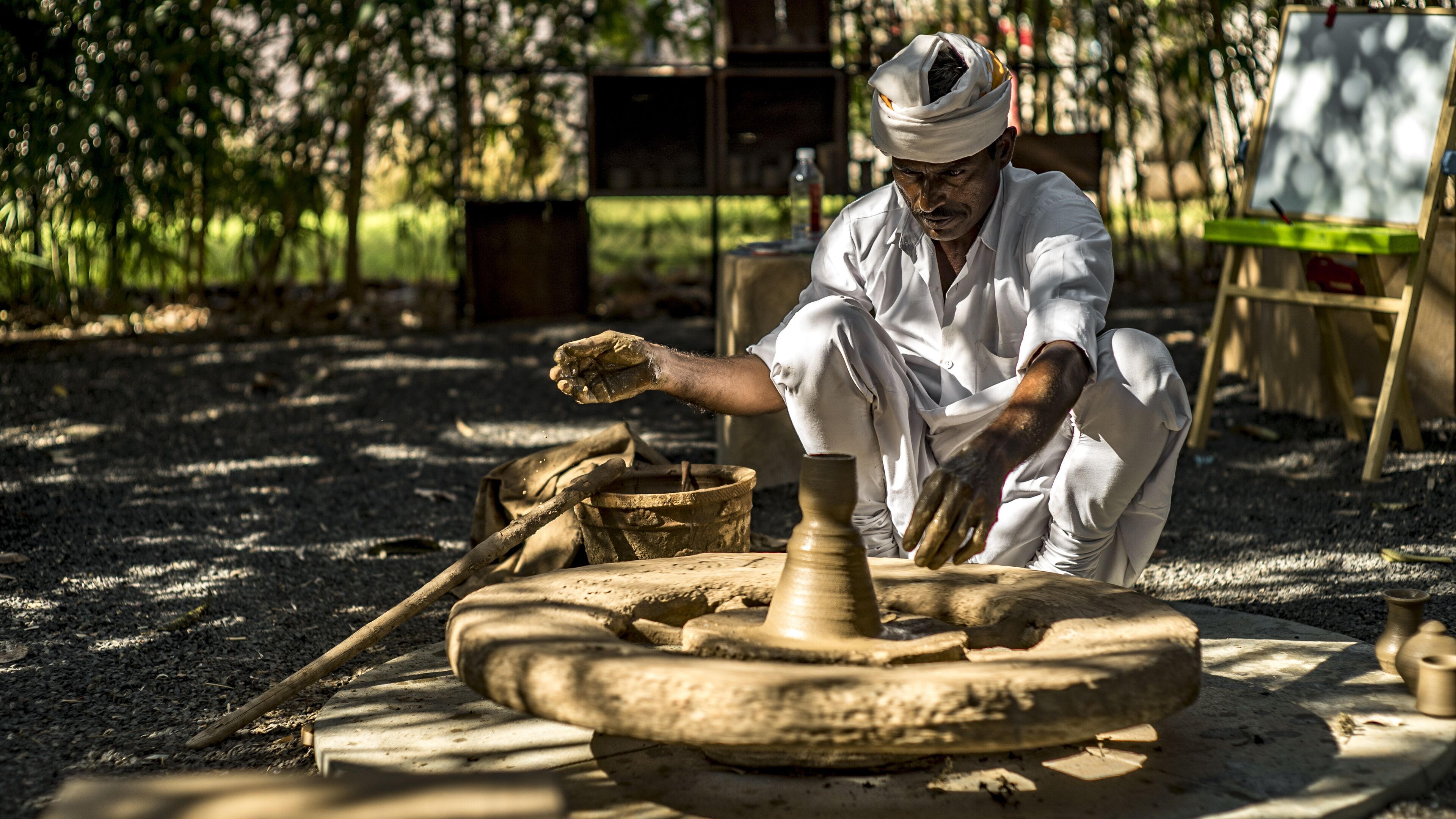 A person working on pottery in an outdoor setting with a wheel and clay.