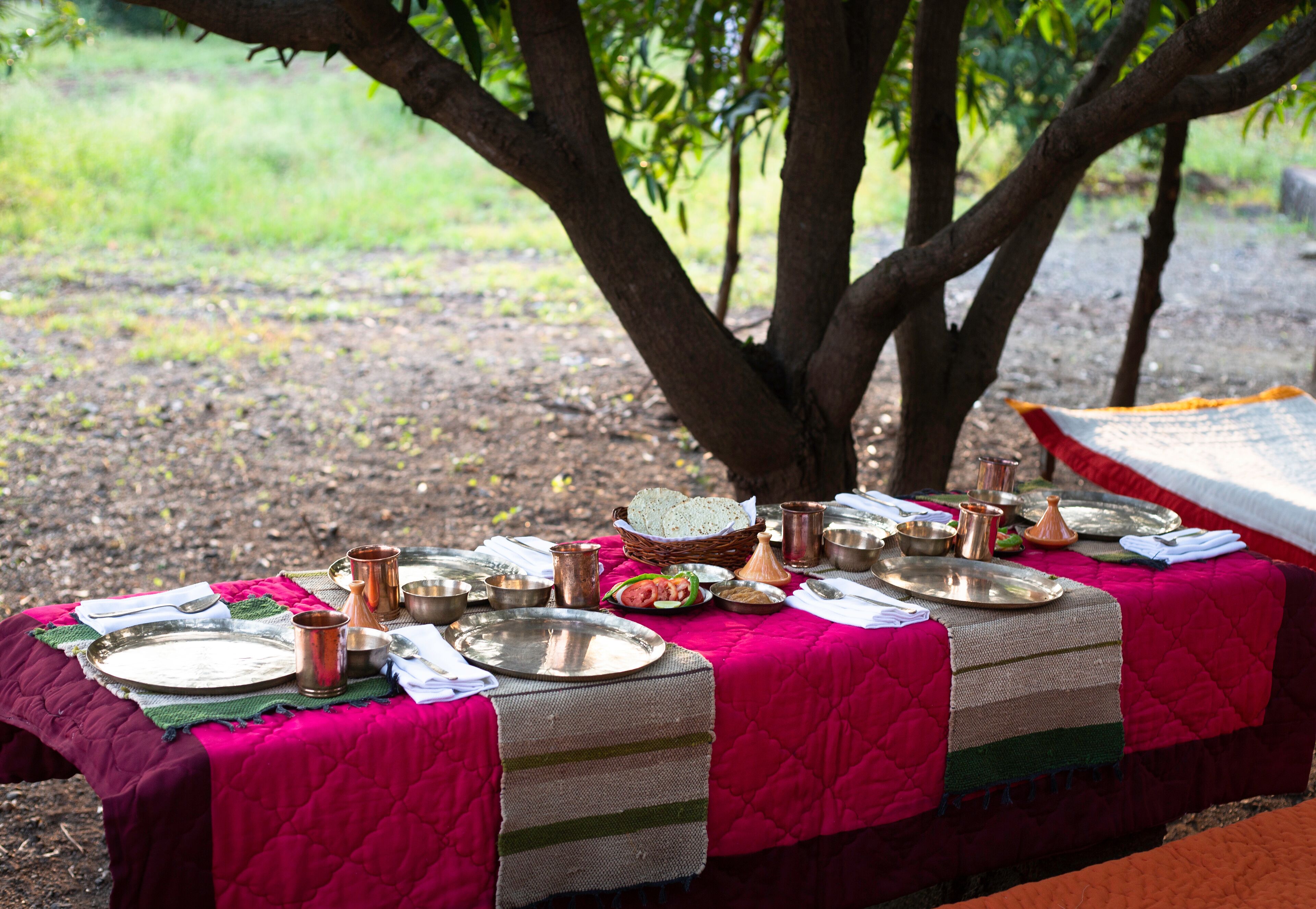 A dining table set outdoors with a vibrant pink tablecloth, various dishes, and utensils.