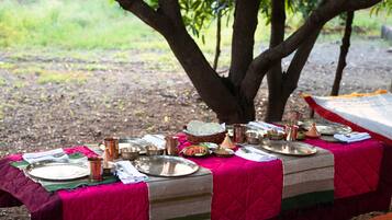 A dining table set outdoors with a vibrant pink tablecloth, various dishes, and utensils.