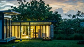 A modern house with large glass windows, a wooden deck, and a lush garden. - Woods at Sasan (Talala)