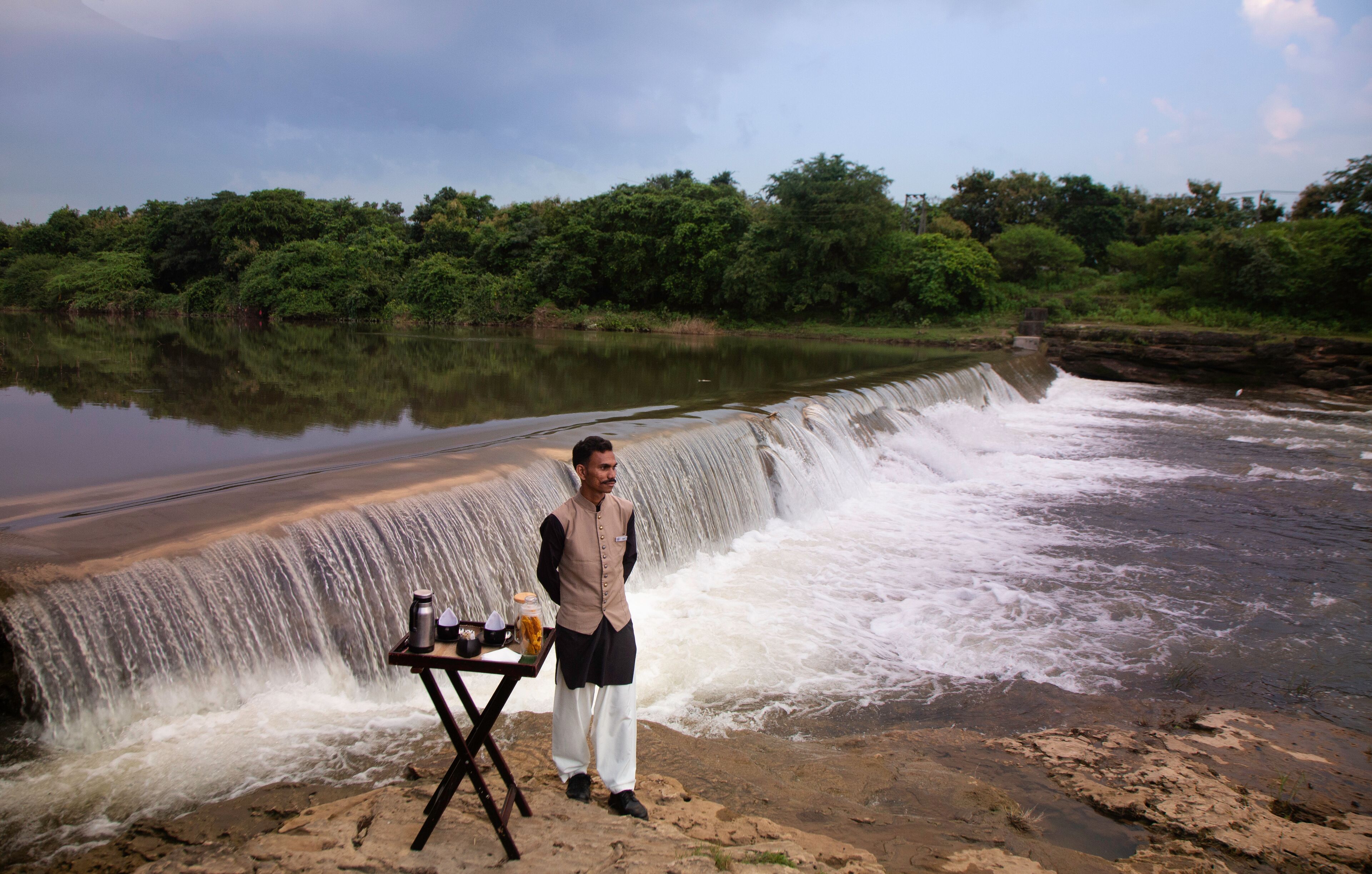 A man standing by a table with a waterfall in the background.