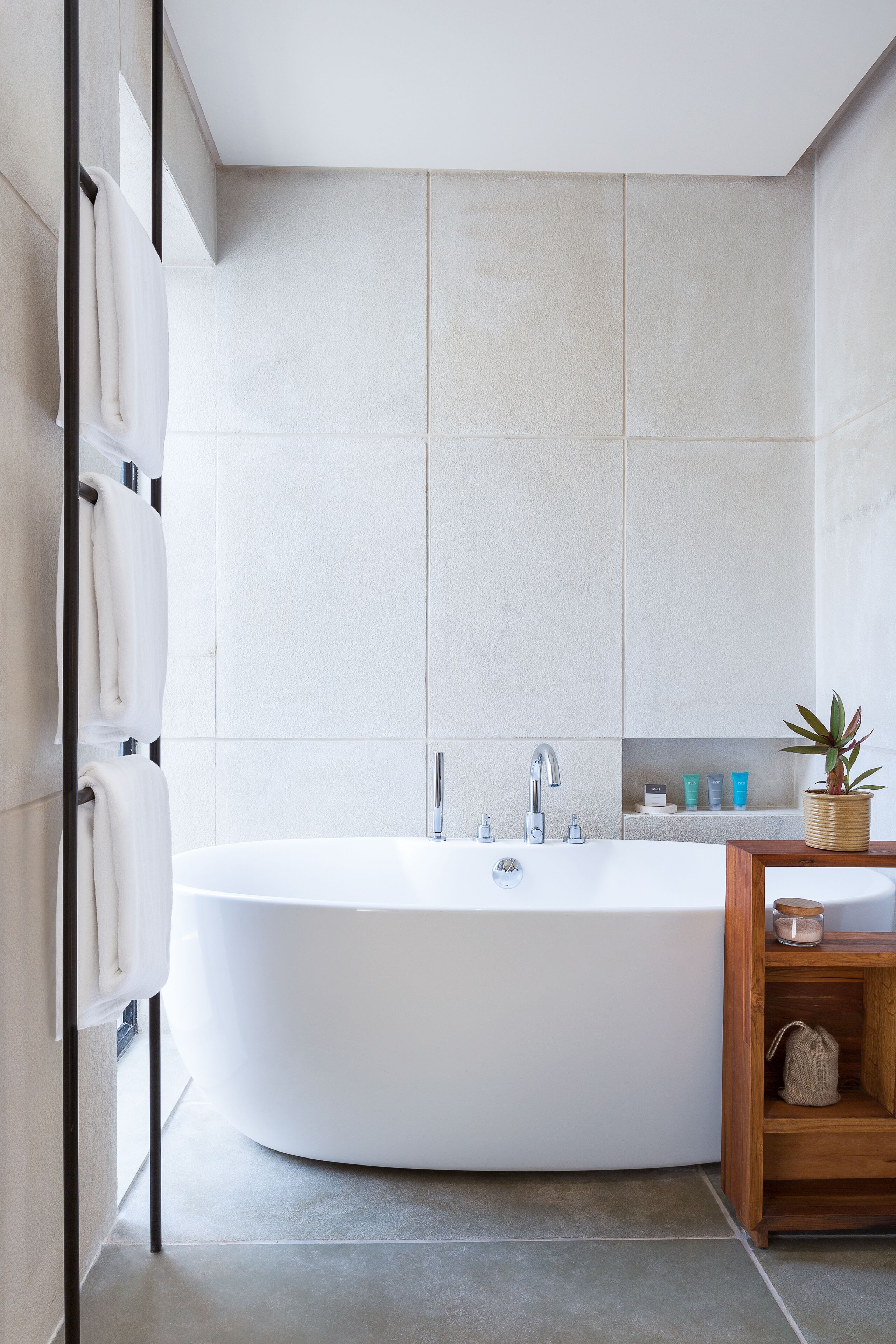 A modern bathroom with a freestanding bathtub, a wooden vanity with a plant, and a towel rack.