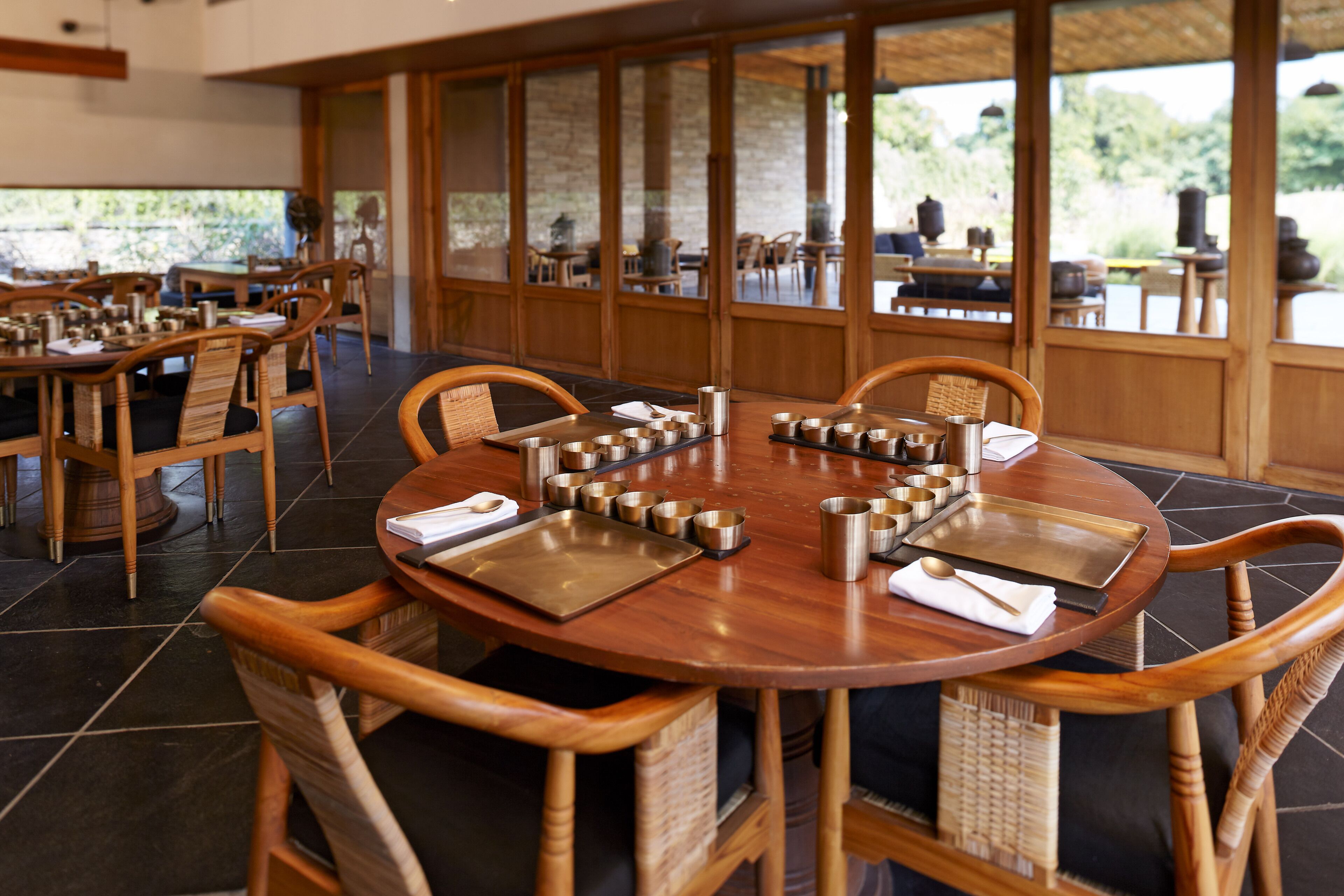 A restaurant with round tables, wooden chairs, and a view of greenery outside.