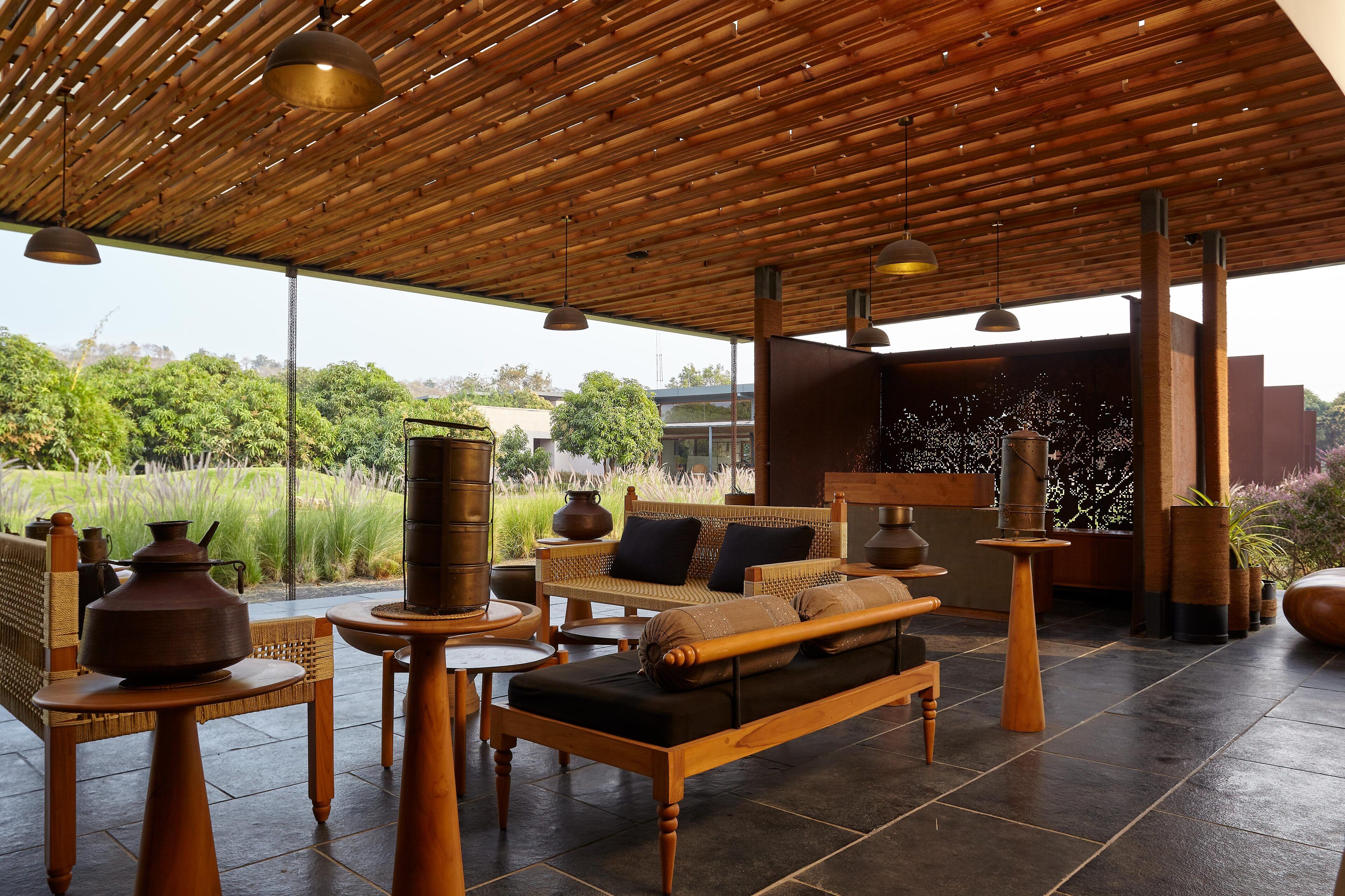 A modern outdoor seating area with a wooden ceiling, wicker furniture, and large windows overlooking a garden.