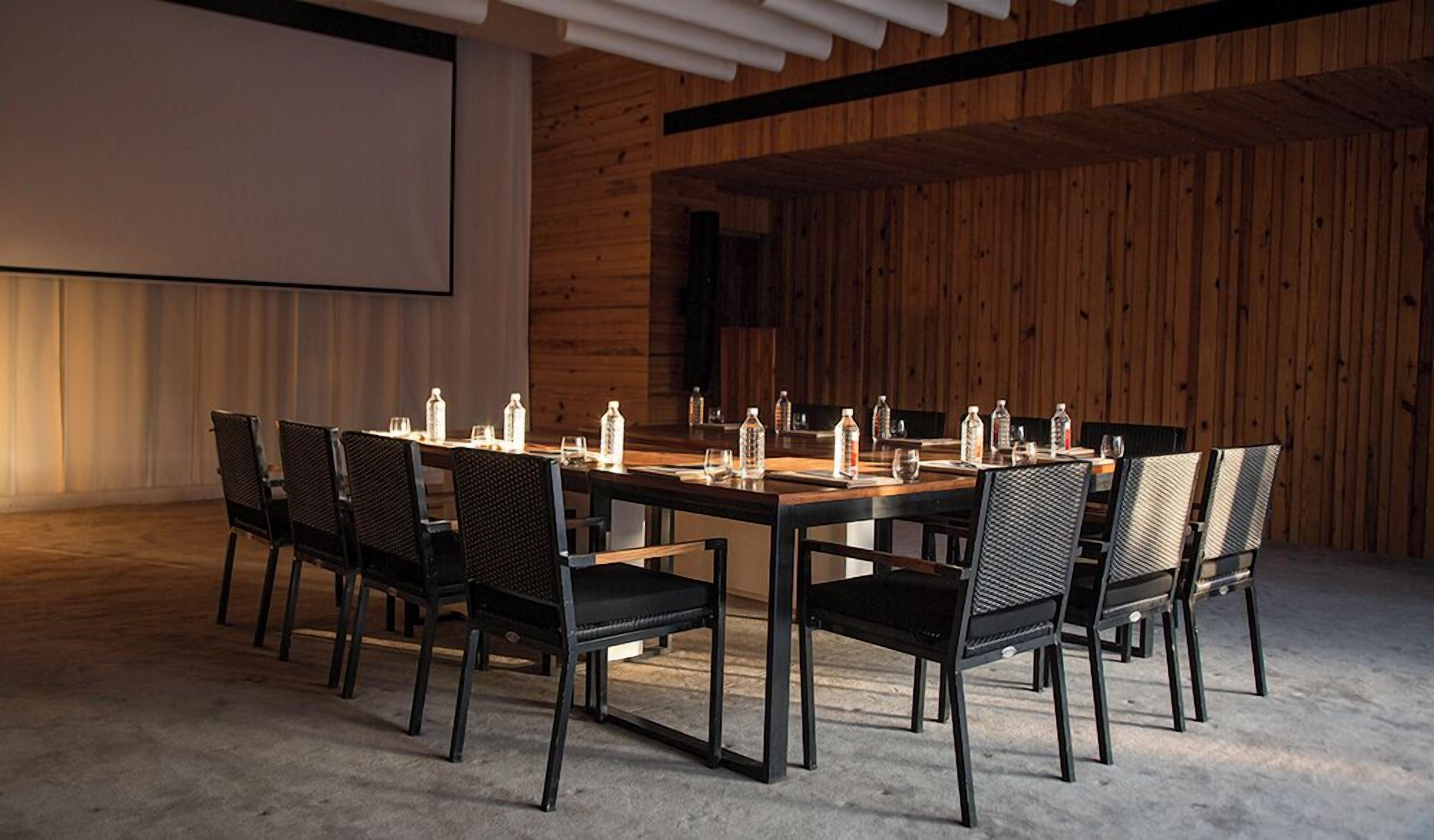 Une salle de conférence avec une longue table, des chaises noires et des bouteilles d’eau posées sur la table.