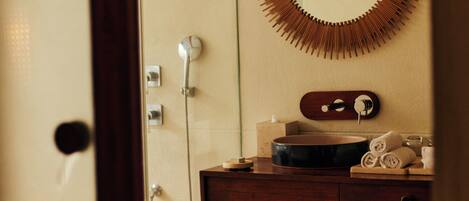 A bathroom with a wooden vanity, a round mirror with a wooden frame, a shower, and a wicker basket on the floor.