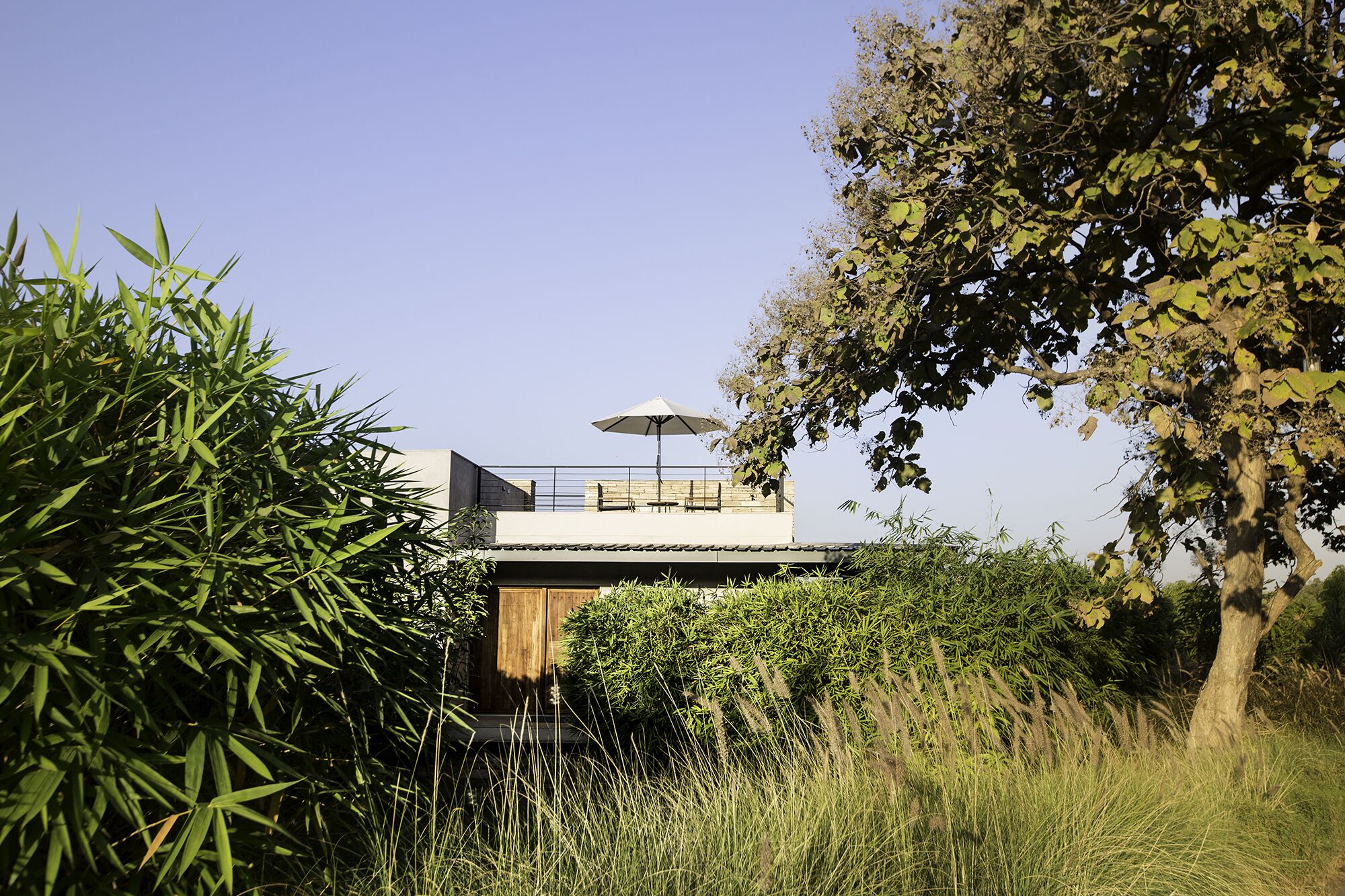 A modern house with a flat roof, a wooden deck, and a large umbrella.