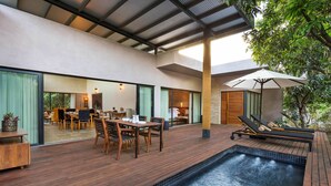A modern outdoor pool area with wooden decking, a lounge chair, and a dining table with chairs. - Woods at Sasan (Talala)