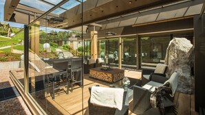 A modern outdoor patio with glass walls, wicker furniture, and a stone fireplace. - Mountain Spa Resort Albion (Castelrotto)