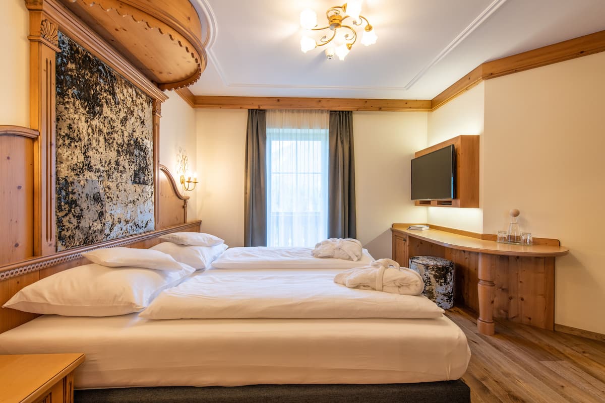 A hotel room with two beds, a wooden headboard, a large mirror, a television, and a small table with a lamp.