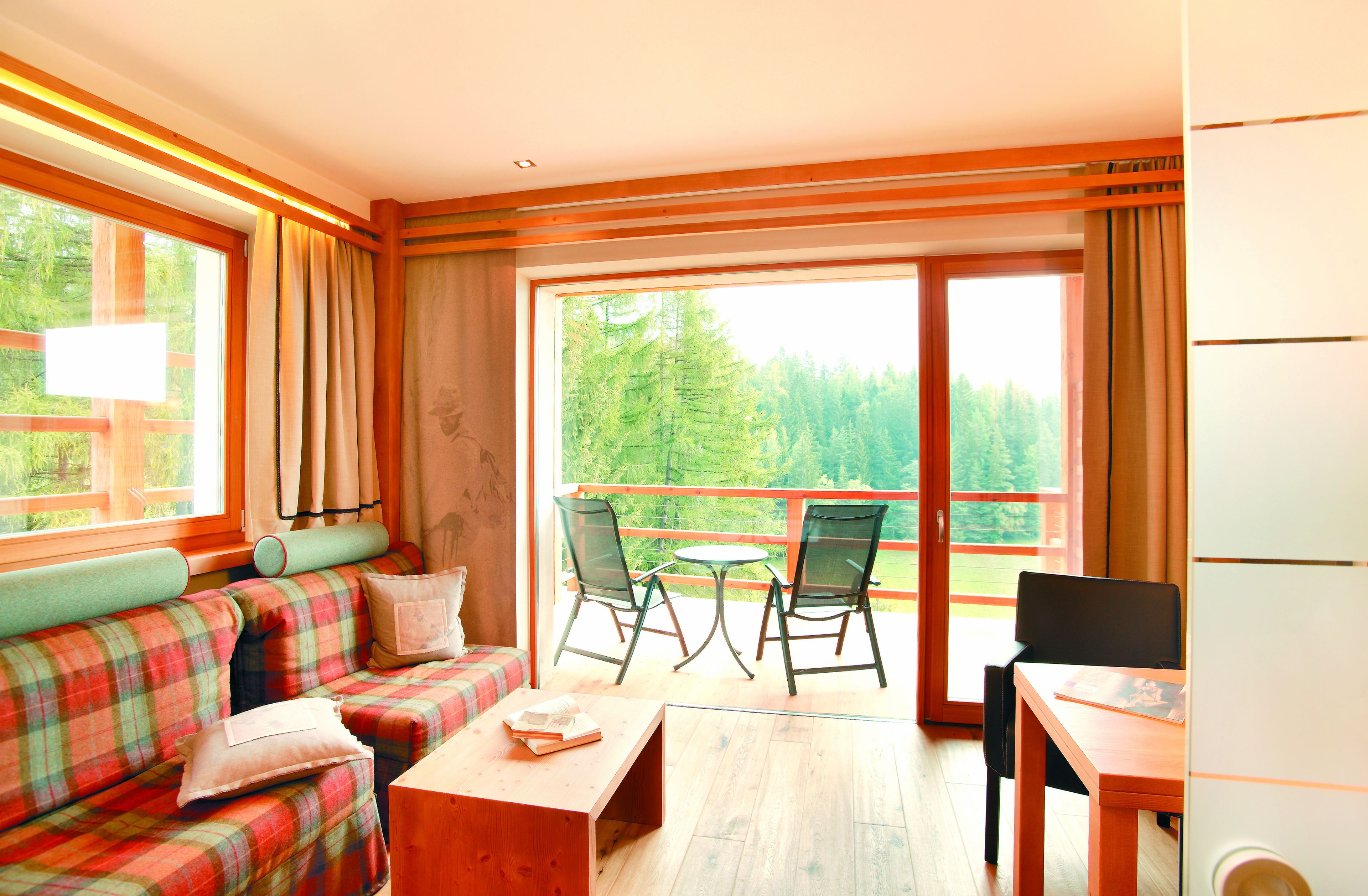 A room with a plaid sofa, a small table, and two chairs. There is a balcony with a view of trees.