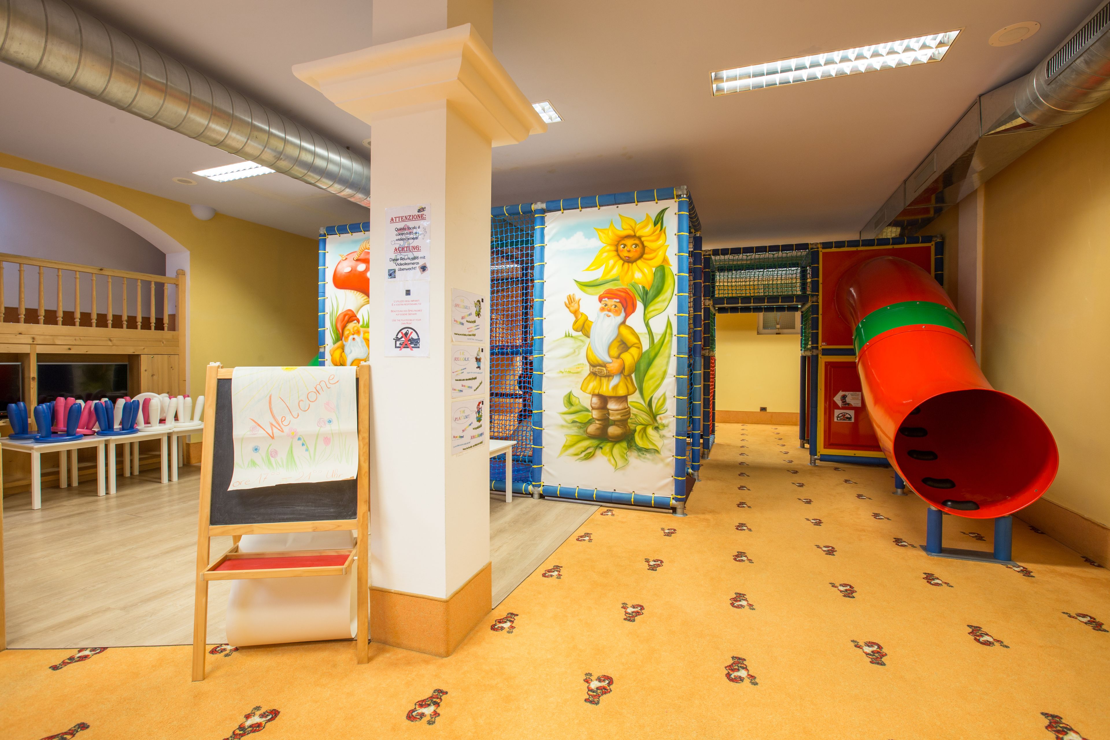 A children's play area with a slide, a welcome mat, and a bulletin board with notices.