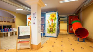 A children's play area with a slide, a welcome mat, and a bulletin board with notices.