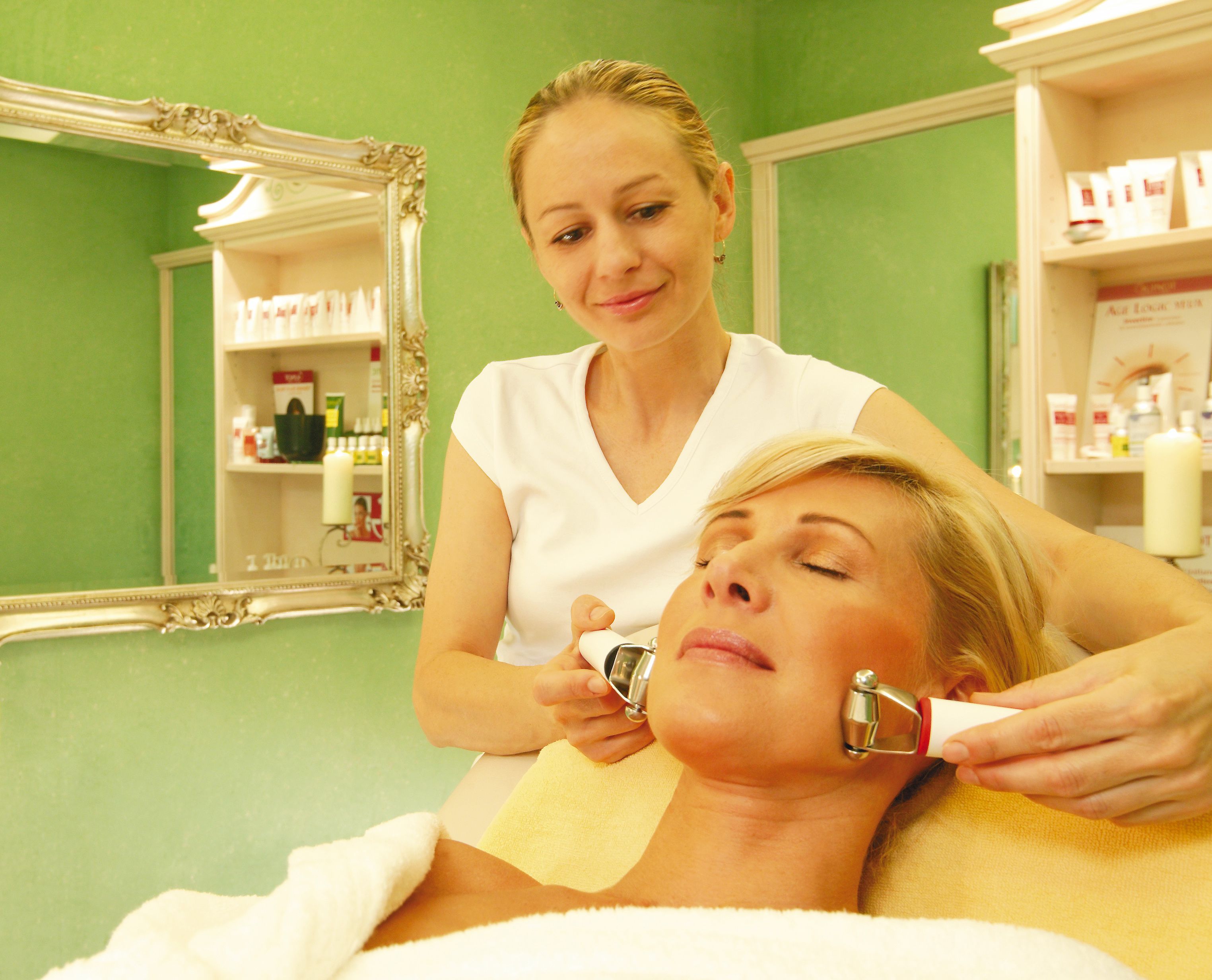 Una persona recibe un tratamiento facial en una habitación con un espejo y estanterías llenas de productos.