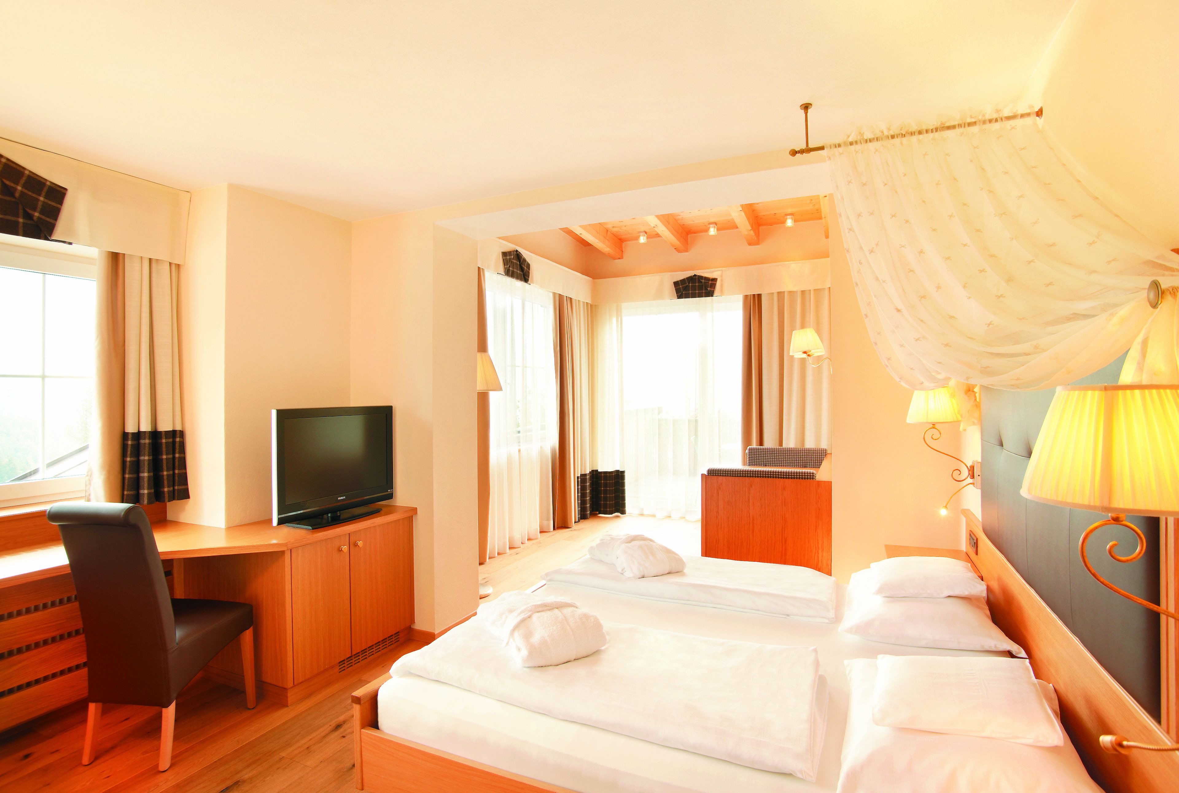A hotel room with a bed, a desk with a television, a chair, and a window with curtains.