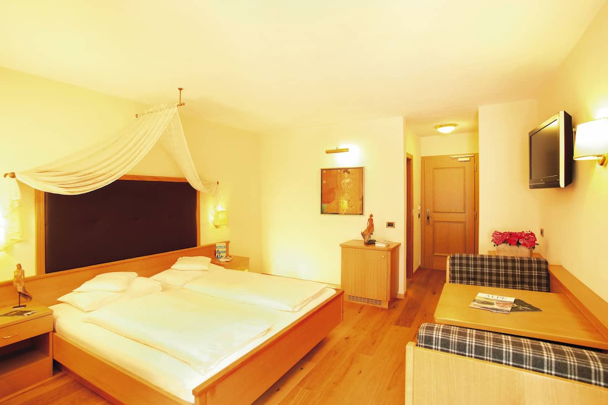 A hotel room with a large bed, bedside tables, a small desk with a chair, a television mounted on the wall, and a door leading to another room.