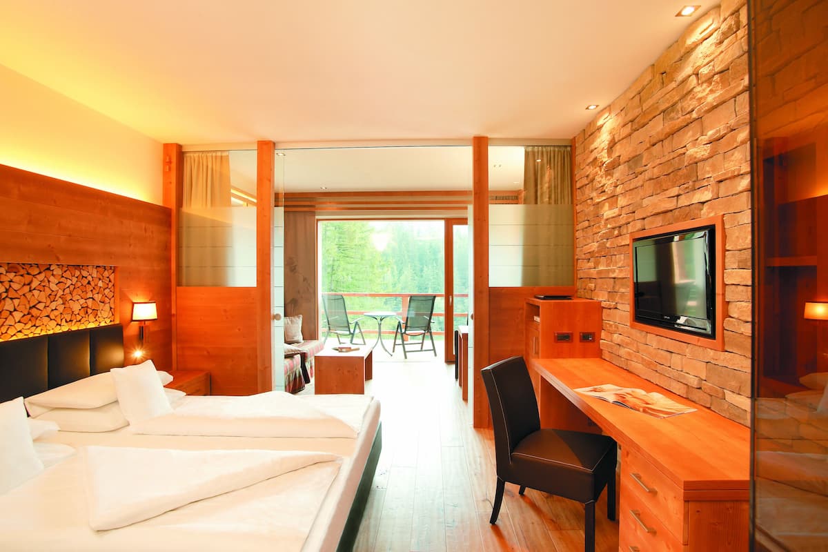A hotel room with a bed, a desk, a TV, and a balcony with a table and chairs.