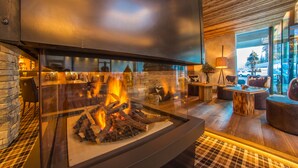A modern interior with a glass fireplace, stone walls, and wooden flooring. - Mountain Spa Resort Albion (Castelrotto)