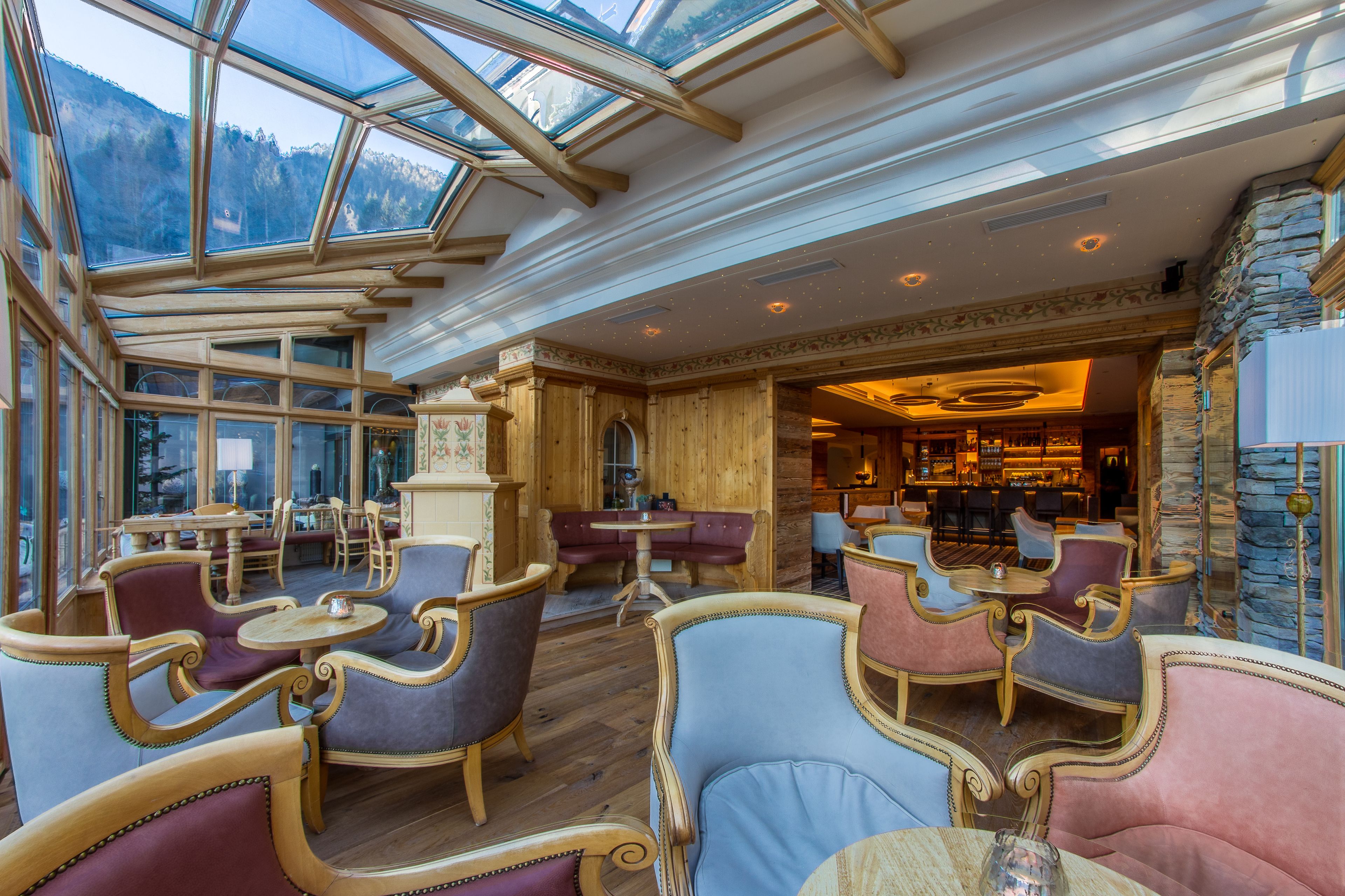 A spacious interior with wooden flooring, multiple seating areas, and a large glass ceiling offering views of the outdoors.