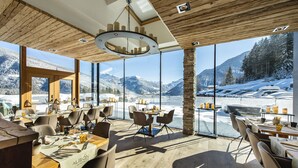 A restaurant with large windows offering mountain views, wooden ceiling, and modern furniture. - Mountain Spa Resort Albion (Castelrotto)