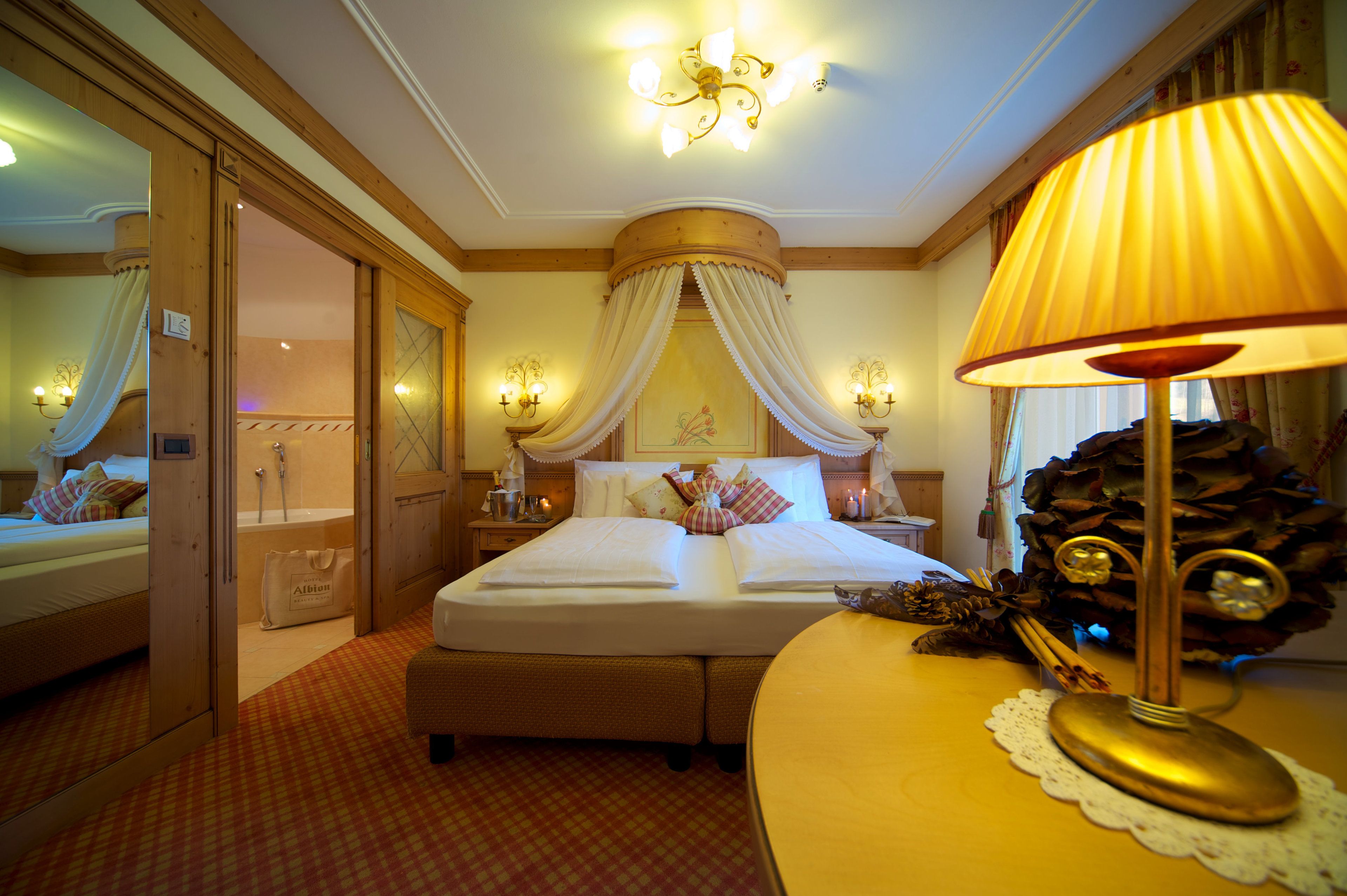 Ein Hotelzimmer mit einem großen Bett, einem Nachttisch mit Lampe, einem Spiegel und einem durch eine offene Tür einsehbaren Badezimmer.