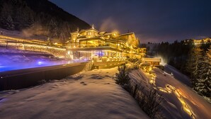 A snow-covered landscape with a large, illuminated building featuring multiple levels and a prominent entrance. - Mountain Spa Resort Albion (Castelrotto)