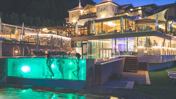 A hotel with a pool area, outdoor seating, and a mountain backdrop. - Mountain Spa Resort Albion (Castelrotto)