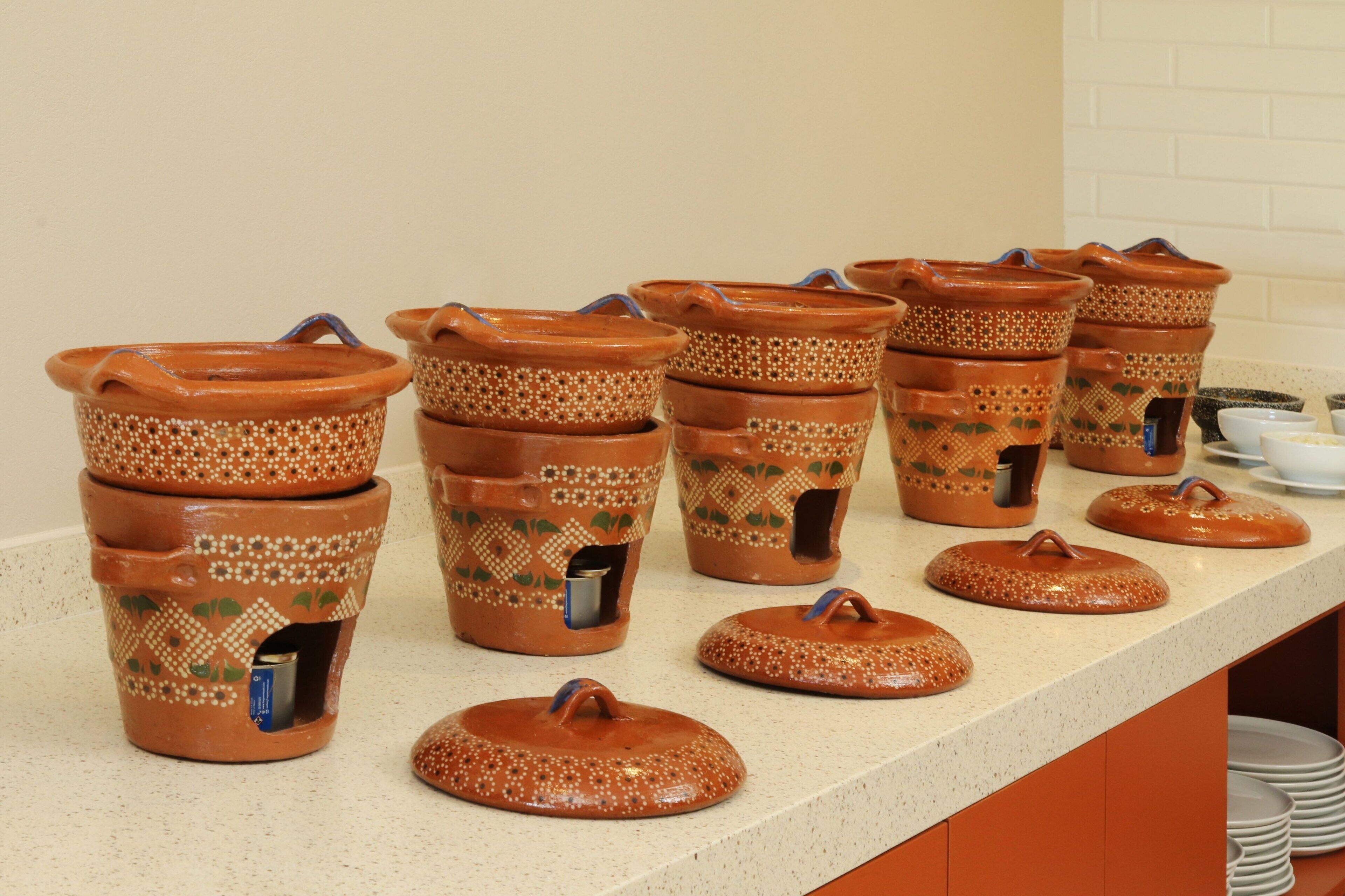 Una encimera de cocina con varios botes de terracota con tapas, algunos con asas y otros con caños, y unos pocos cuencos pequeños.