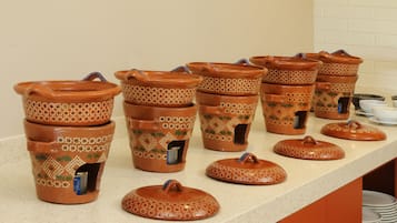 Una encimera de cocina con varios botes de terracota con tapas, algunos con asas y otros con caños, y unos pocos cuencos pequeños.