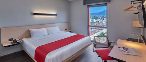 Habitación de hotel moderna con una cama grande, un escritorio, una silla, un televisor y una ventana con vista a la ciudad.